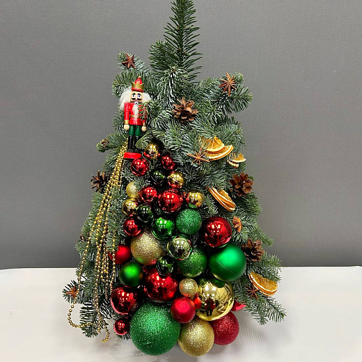 Елка из нобилиса с разноцветным декором и щелкунчиком по лучшей цене в Москве Елка из нобилиса с разноцветным декором и щелкунчиком с доставкой в Москве