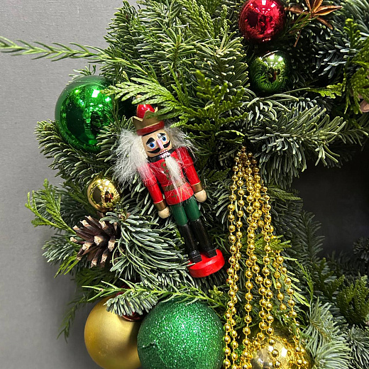 Новогодний венок с разноцветным декором и Щелкунчиком по лучшей цене в Москве Новогодний венок с разноцветным декором и Щелкунчиком с доставкой в Москве